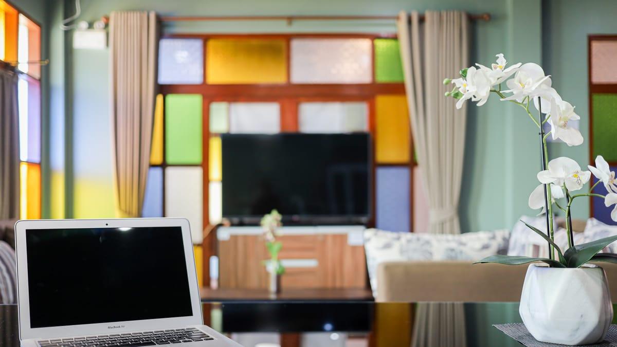 Open laptop on a glass table in a lounge with stained glass windows at Jintara Rehab in Chiang Mai